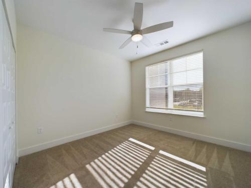 Three Bedroom Apartment Sailor Apt. 1-201Apartments in for rent Farragut TN Empty room with beige carpet, white walls, a ceiling fan, and sunlight streaming through a large window with blinds. Door on the left side. Anchor 934 Apartments in Biddle Farms Town Center