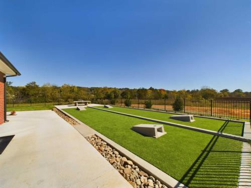 Apartments in for rent Farragut TN Backyard with bocce ball court, stone pathways, and a wooden bench, surrounded by a metal fence and trees in the background under a clear blue sky. Anchor 934 Apartments in Biddle Farms Town Center