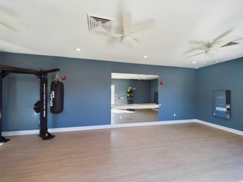 Apartments in for rent Farragut TN Empty gym room with wood flooring, blue walls, and ceiling fans. Contains a punching bag, wall mirror, and electronic sign. Anchor 934 Apartments in Biddle Farms Town Center