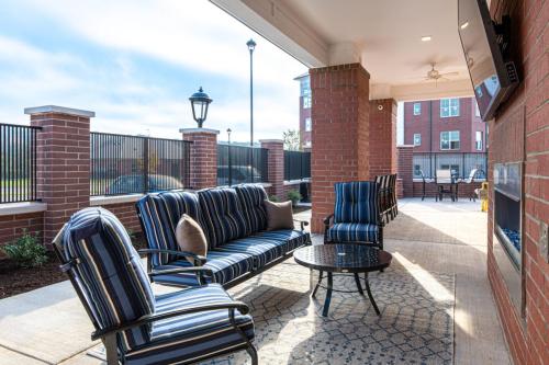 Apartments in for rent Farragut TN Outdoor patio with blue-striped cushioned furniture, a round coffee table, and a flatscreen TV mounted on a brick wall. Nearby are brick columns and a black fence. Anchor 934 Apartments in Biddle Farms Town Center