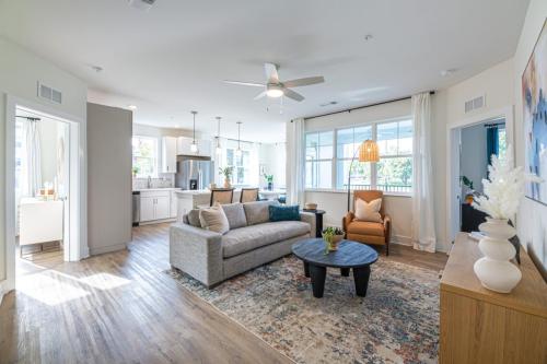 Apartments in for rent Farragut TN Modern living room with a gray sofa, armchair, round coffee table, and large window. Open-space layout leading to a kitchen with white cabinets and a dining area. Wood flooring throughout. Anchor 934 Apartments in Biddle Farms Town Center