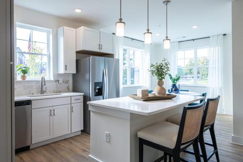 Apartments in for rent Farragut TN A modern kitchen with white cabinets, stainless steel appliances, and a central island with bar stools. Large windows provide natural light. Anchor 934 Apartments in Biddle Farms Town Center