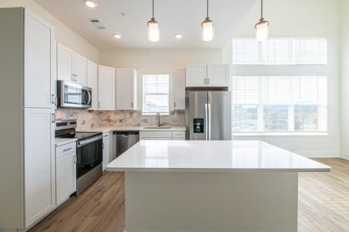 Apartments in for rent Farragut TN Modern kitchen with white cabinetry, stainless steel appliances, an island, and wooden flooring. Large windows provide natural light. Anchor 934 Apartments in Biddle Farms Town Center