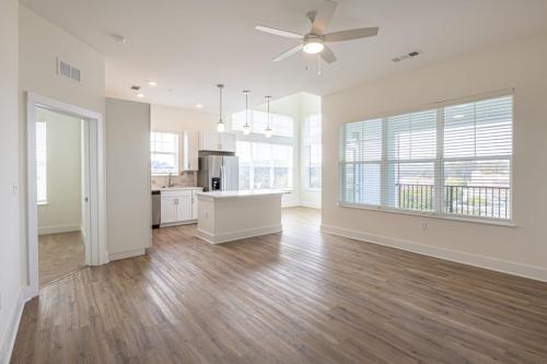 Apartments in for rent Farragut TN Open-concept living area with hardwood floors, white kitchen cabinets, ceiling fan, and large windows. Adjacent room visible on the left. Anchor 934 Apartments in Biddle Farms Town Center