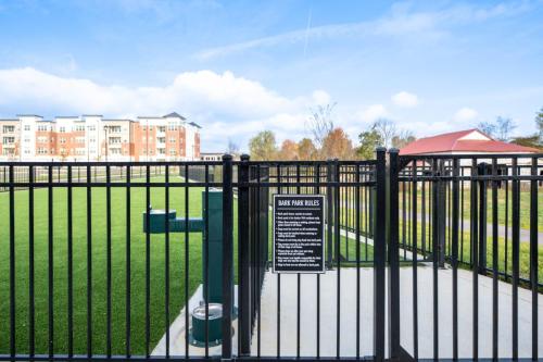 Apartments in for rent Farragut TN A gated dog park entrance with posted rules, surrounded by grass, an apartment building, and a red-roofed structure in the background. Anchor 934 Apartments in Biddle Farms Town Center