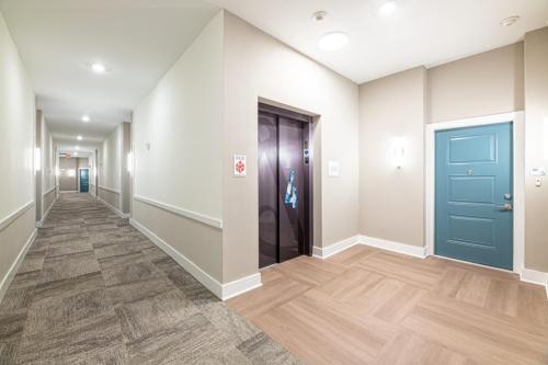 Apartments in for rent Farragut TN A well-lit hallway with an elevator and a closed blue door, featuring neutral-colored walls and carpeted flooring. Anchor 934 Apartments in Biddle Farms Town Center