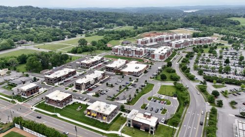 Biddle Farms Farragut Town Center Apartments in for rent Farragut TN Aerial view of Biddle Farms Farragut Town Center, a suburban shopping and residential complex surrounded by roads, parking lots, trees, and distant hills. Anchor 934 Apartments in Biddle Farms Town Center